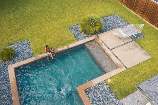 Overhead view of family sitting on the edge of a swimming pool in the backyard